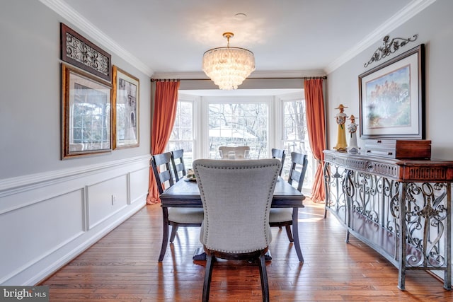 dining room with a wainscoted wall, a decorative wall, an inviting chandelier, ornamental molding, and wood finished floors