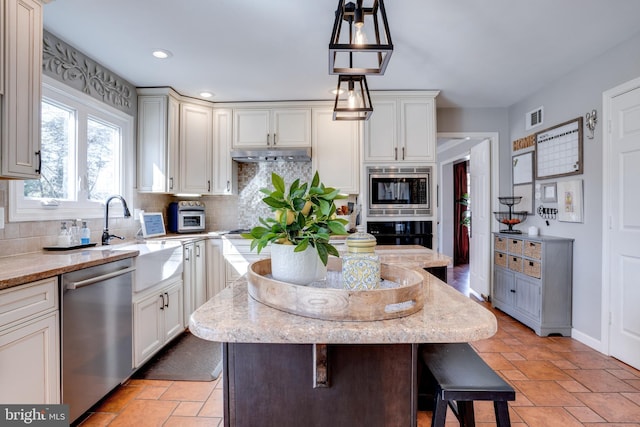 kitchen with visible vents, backsplash, appliances with stainless steel finishes, a kitchen island, and under cabinet range hood