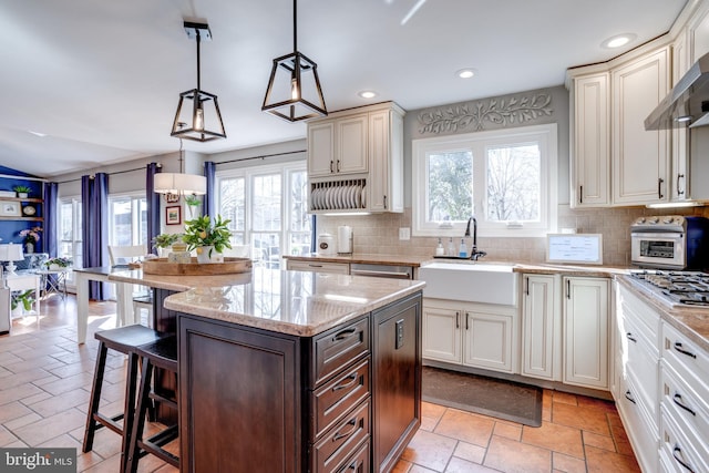 kitchen featuring tasteful backsplash, a kitchen breakfast bar, stone tile flooring, wall chimney range hood, and a sink