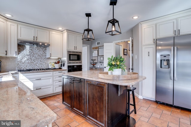 kitchen with stone tile floors, white cabinets, decorative backsplash, stainless steel appliances, and under cabinet range hood