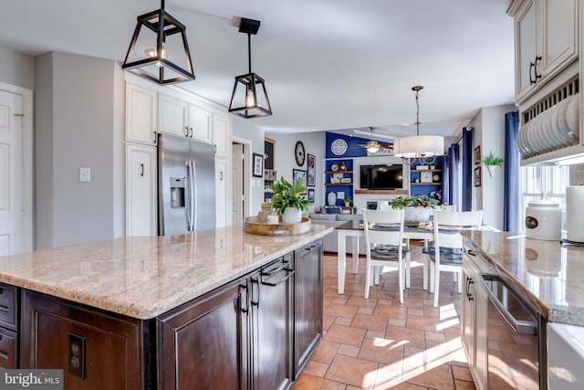 kitchen with dark brown cabinetry, stainless steel fridge with ice dispenser, stone finish floor, a center island, and light stone countertops