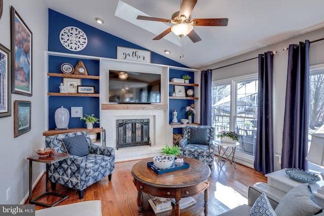 living room with built in shelves, wood finished floors, a ceiling fan, vaulted ceiling, and a brick fireplace