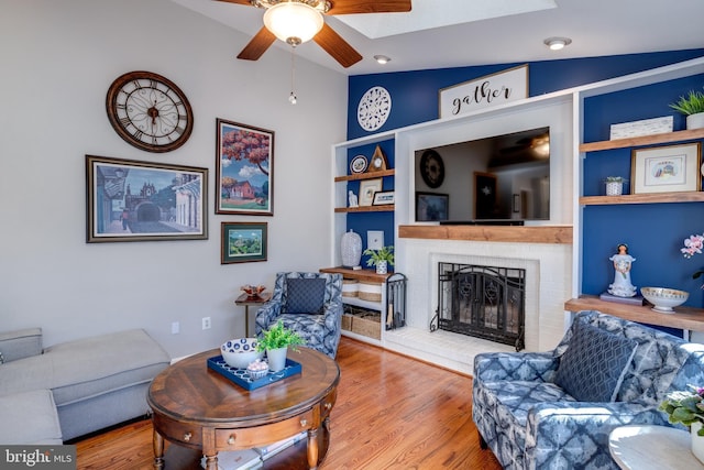 living room with ceiling fan, lofted ceiling, a fireplace, and wood finished floors