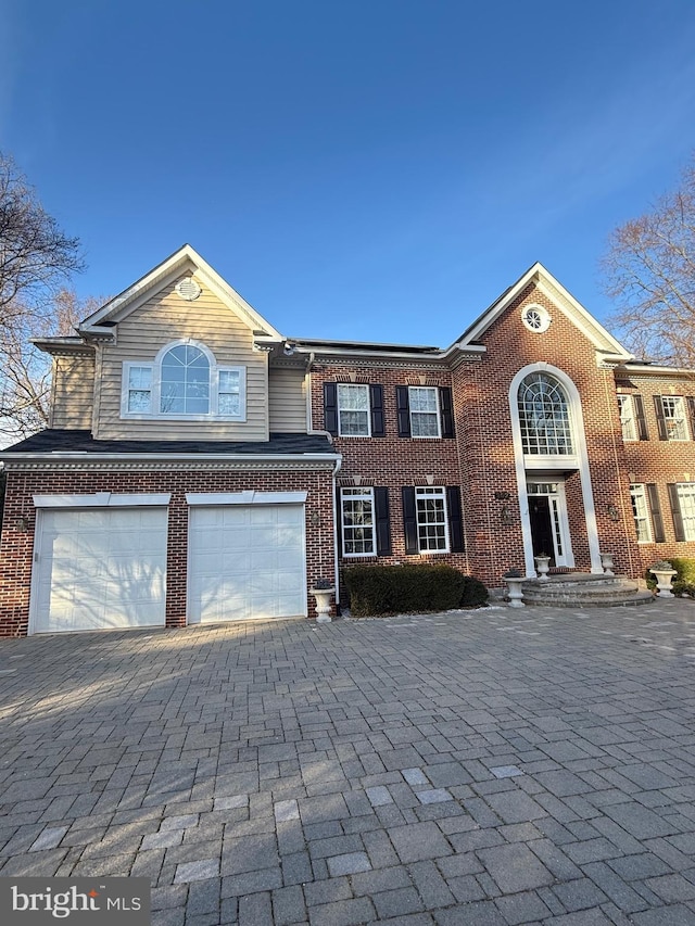 view of front of property featuring decorative driveway, brick siding, and an attached garage