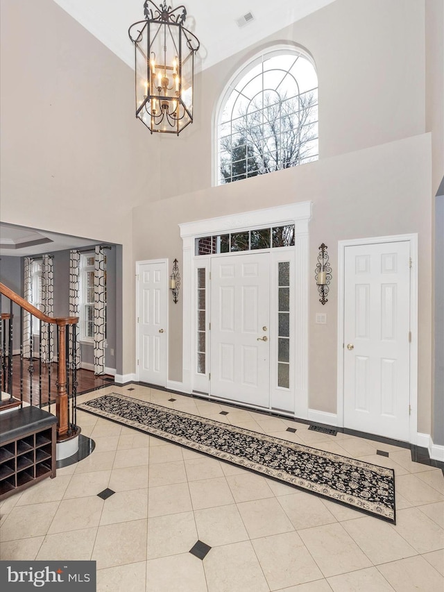 tiled entryway with a chandelier, a towering ceiling, visible vents, stairs, and baseboards