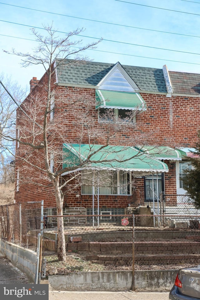 view of front of property with a fenced front yard, roof with shingles, and brick siding