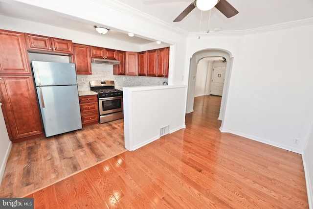 kitchen with arched walkways, light wood finished floors, stainless steel appliances, light countertops, and under cabinet range hood