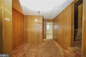 hallway featuring wood walls, carpet, and an inviting chandelier