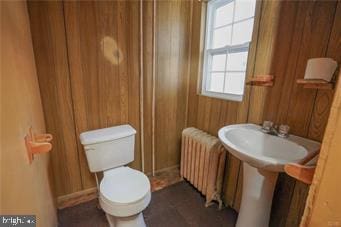 half bath with toilet, wood walls, and radiator heating unit