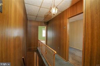 corridor featuring carpet, wooden walls, and a drop ceiling