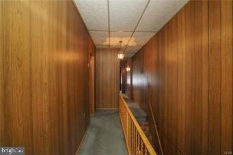 hall featuring wooden walls and a drop ceiling