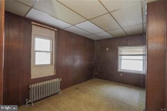 unfurnished room featuring radiator, wood walls, and a wealth of natural light