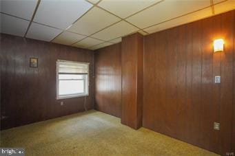 spare room featuring light carpet, a drop ceiling, and wooden walls