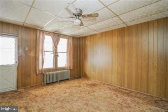 carpeted spare room with wood walls, radiator heating unit, a paneled ceiling, and a ceiling fan