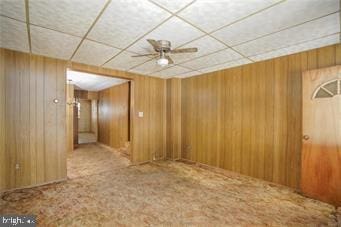 spare room with a drop ceiling, wood walls, carpet flooring, and ceiling fan