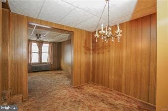 empty room featuring radiator heating unit, wood walls, carpet, and an inviting chandelier