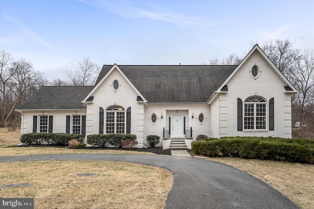 french country home with driveway, brick siding, a shingled roof, and a front yard