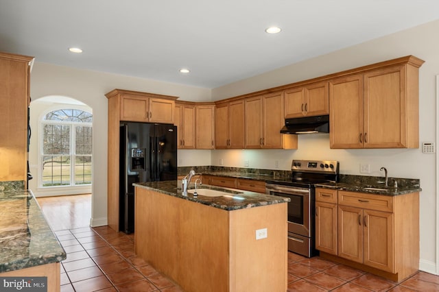 kitchen featuring a sink, dark stone counters, under cabinet range hood, stainless steel electric range, and black fridge