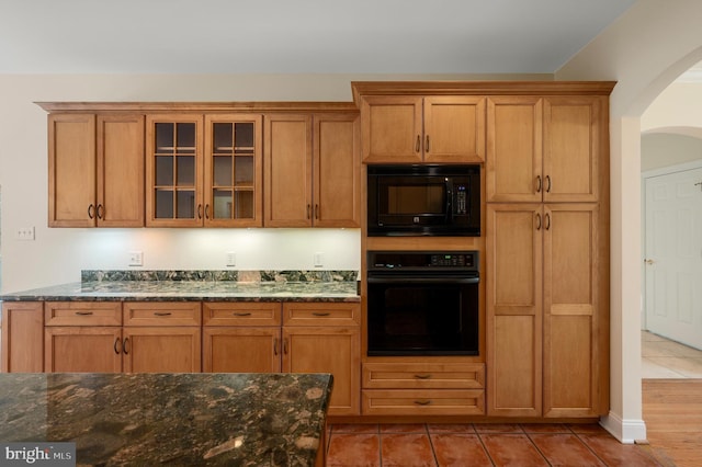 kitchen with dark stone counters, black appliances, and glass insert cabinets