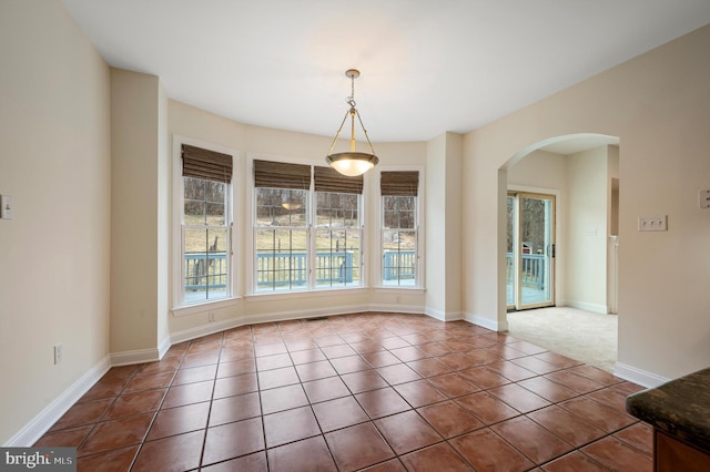 unfurnished dining area with arched walkways, plenty of natural light, and tile patterned floors