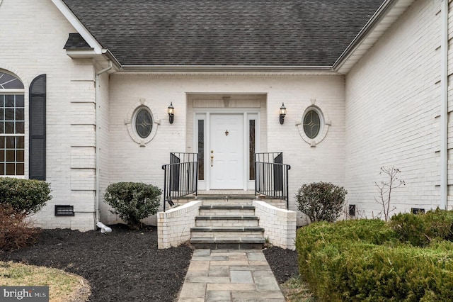 entrance to property featuring crawl space, roof with shingles, and brick siding