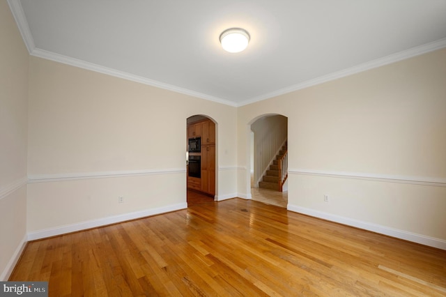 unfurnished room featuring light wood-style floors, baseboards, arched walkways, and ornamental molding