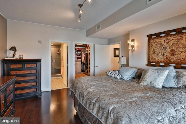 bedroom featuring ensuite bathroom, dark wood-type flooring, visible vents, a closet, and a walk in closet