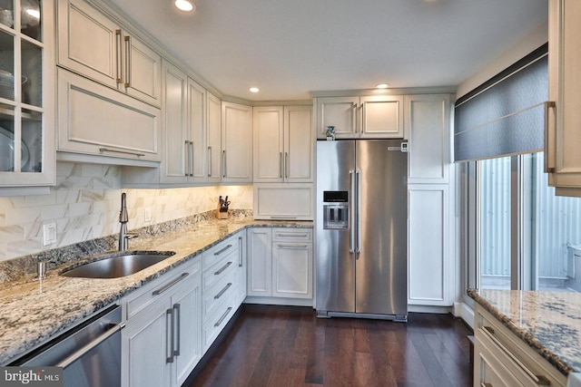 kitchen with stainless steel appliances, a sink, glass insert cabinets, and light stone countertops