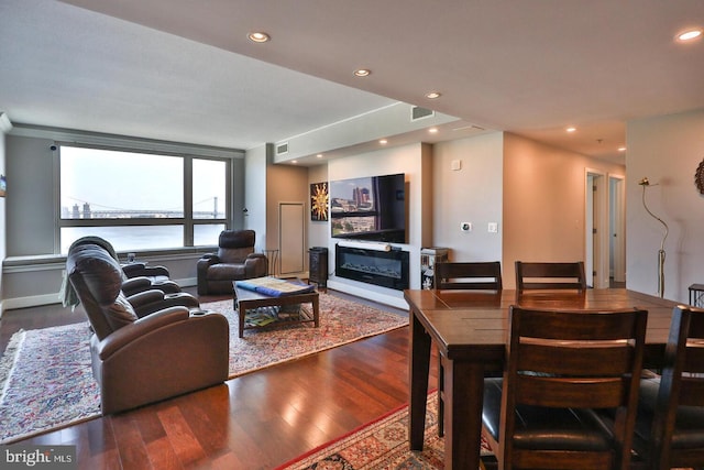 living room with dark wood-style floors, a glass covered fireplace, visible vents, and recessed lighting