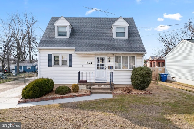 new england style home with roof with shingles, fence, and a front lawn