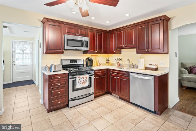 kitchen with reddish brown cabinets, light countertops, appliances with stainless steel finishes, and a sink