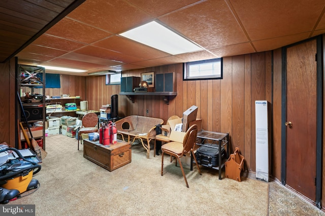 basement featuring carpet flooring, wooden walls, and a drop ceiling