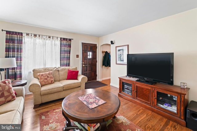 living area featuring arched walkways, wood finished floors, and baseboards