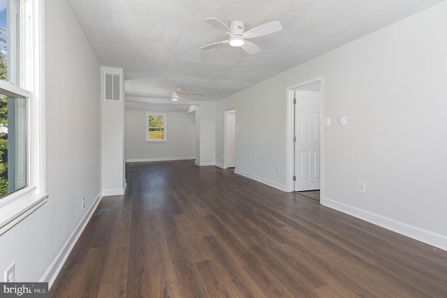 empty room with ceiling fan, a textured ceiling, dark wood-type flooring, visible vents, and baseboards