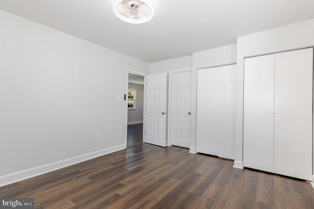 unfurnished bedroom with dark wood-style flooring, multiple closets, and baseboards