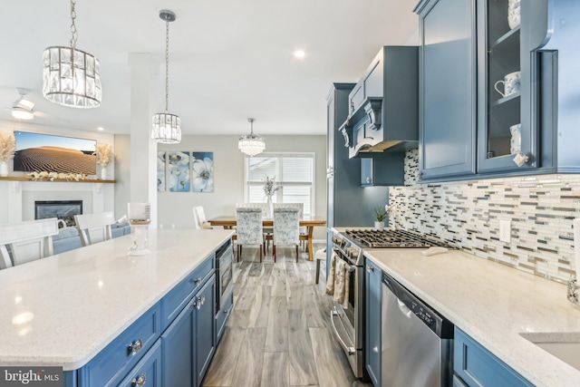 kitchen with a glass covered fireplace, appliances with stainless steel finishes, glass insert cabinets, hanging light fixtures, and blue cabinetry