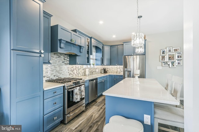 kitchen with decorative light fixtures, blue cabinetry, appliances with stainless steel finishes, glass insert cabinets, and a kitchen island