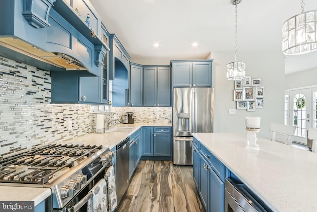 kitchen with decorative backsplash, appliances with stainless steel finishes, blue cabinets, premium range hood, and pendant lighting