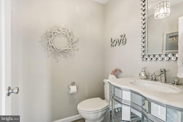 half bath with toilet, baseboards, and vanity