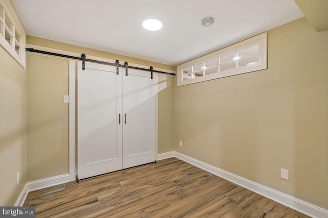 unfurnished bedroom featuring a barn door, a closet, wood finished floors, and baseboards