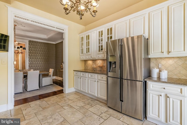 kitchen featuring stone tile floors, a notable chandelier, baseboards, stainless steel fridge, and crown molding