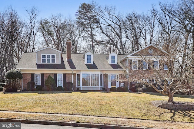 view of front facade with a front yard, a chimney, brick siding, and a shingled roof