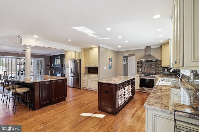 kitchen featuring an island with sink, cream cabinets, stainless steel appliances, and wall chimney exhaust hood