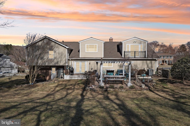 back of property at dusk featuring fence, a lawn, french doors, a balcony, and a patio area