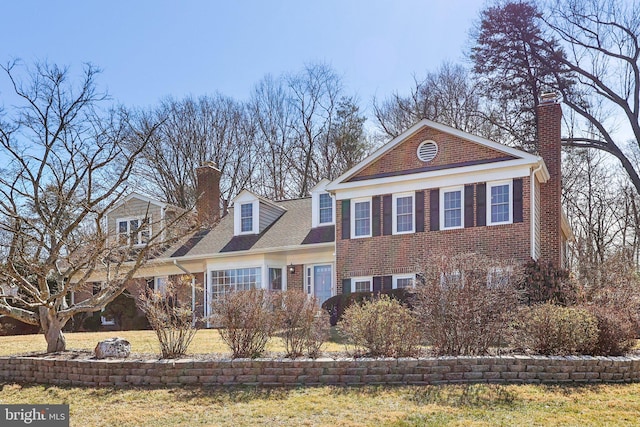 traditional-style house featuring brick siding, roof with shingles, and a chimney