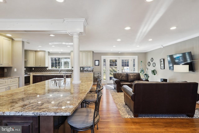 kitchen with light stone countertops, open floor plan, a kitchen bar, cream cabinets, and ornate columns