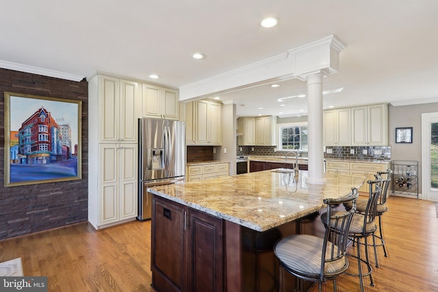 kitchen featuring crown molding, light stone countertops, stainless steel refrigerator with ice dispenser, cream cabinetry, and ornate columns