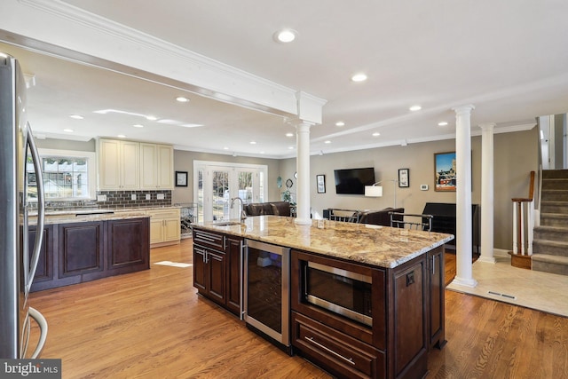 kitchen featuring beverage cooler, appliances with stainless steel finishes, cream cabinetry, ornate columns, and a sink