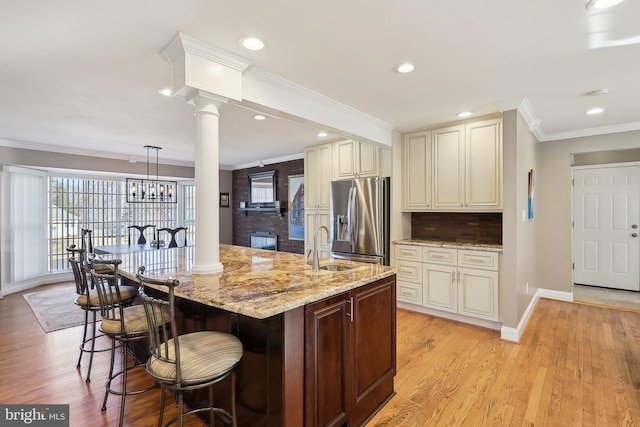 kitchen with a sink, crown molding, stainless steel refrigerator with ice dispenser, and light stone countertops