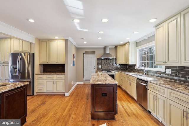 kitchen with crown molding, appliances with stainless steel finishes, cream cabinetry, wall chimney exhaust hood, and a sink